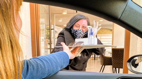 Frau mit Mundschutz reicht Tablett ins Auto 