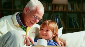 Ein älterer Herr liest einem Kind etwas aus einem Buch vor. 